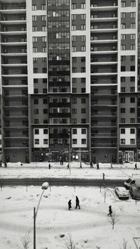 Snow-covered street with pedestrians in front of a modern high-rise building.