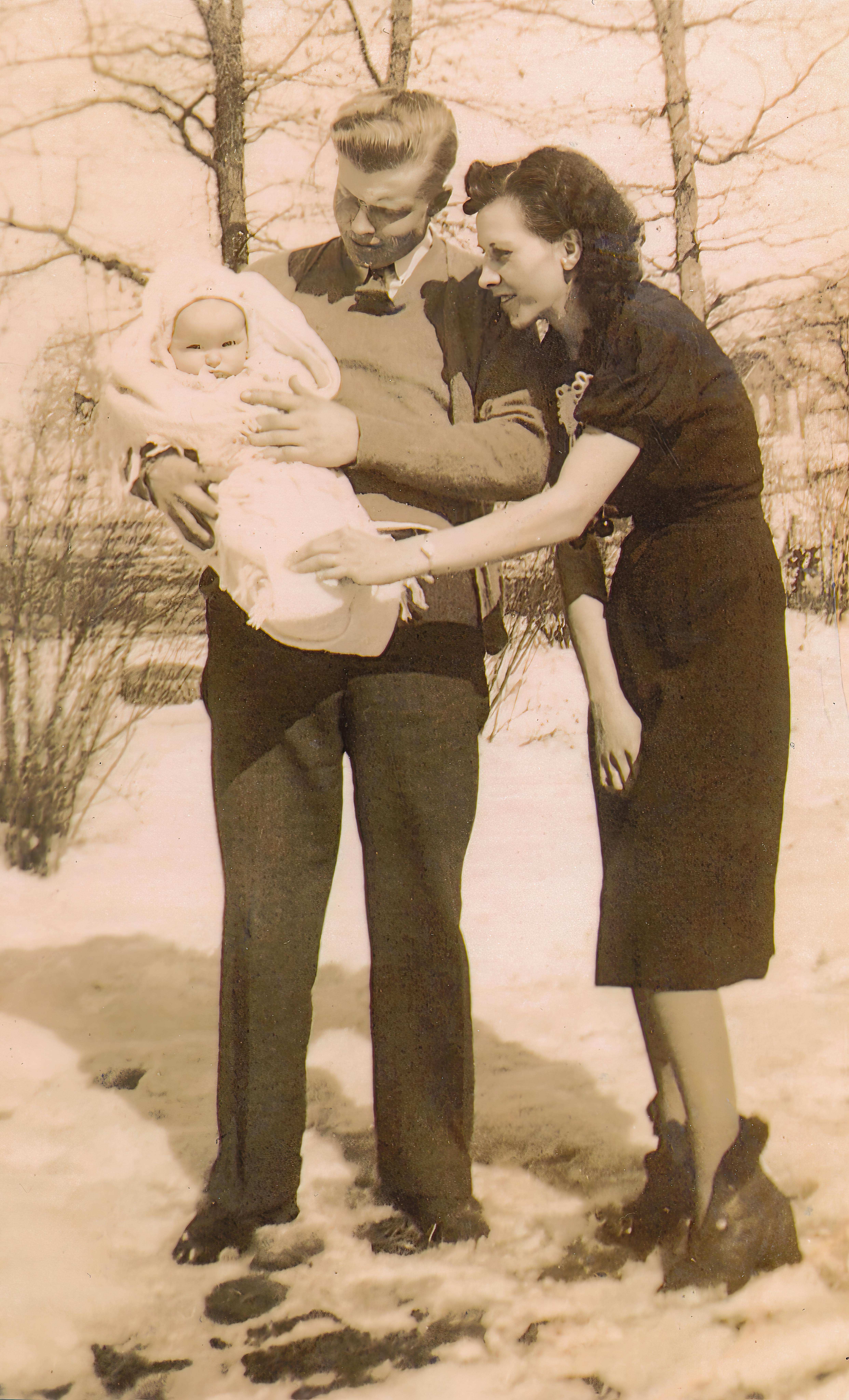 A classic vintage family portrait of parents with their newborn child in a snowy winter setting.