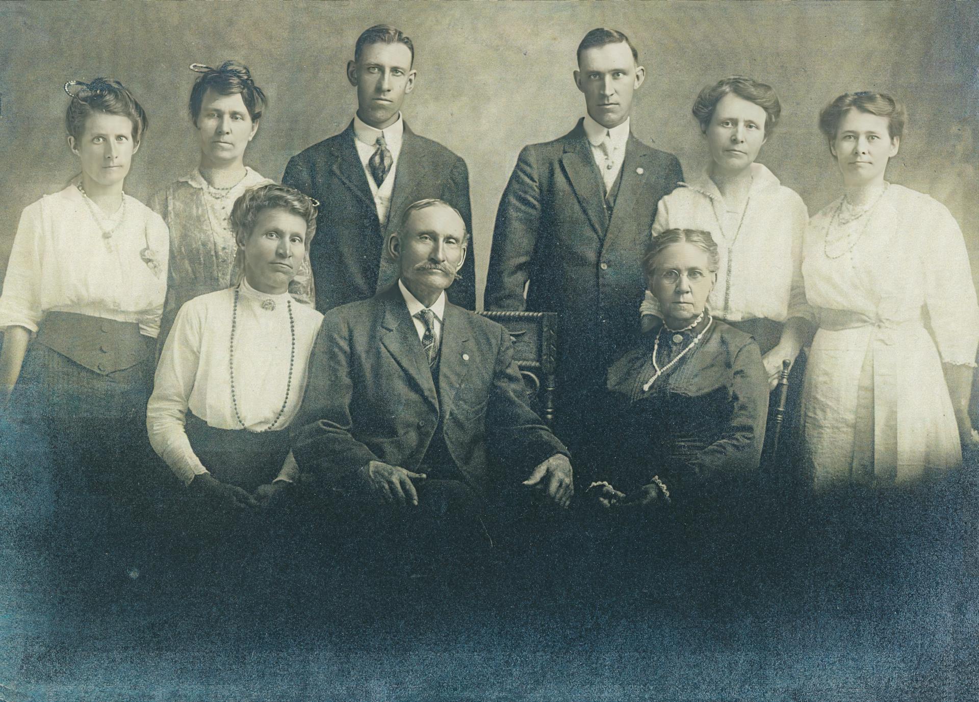 Retro family portrait with seven adults in early 1900s attire.