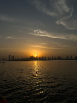 Breathtaking sunset view of Dubai's skyline with the Burj Khalifa, casting reflections on the waterfront.