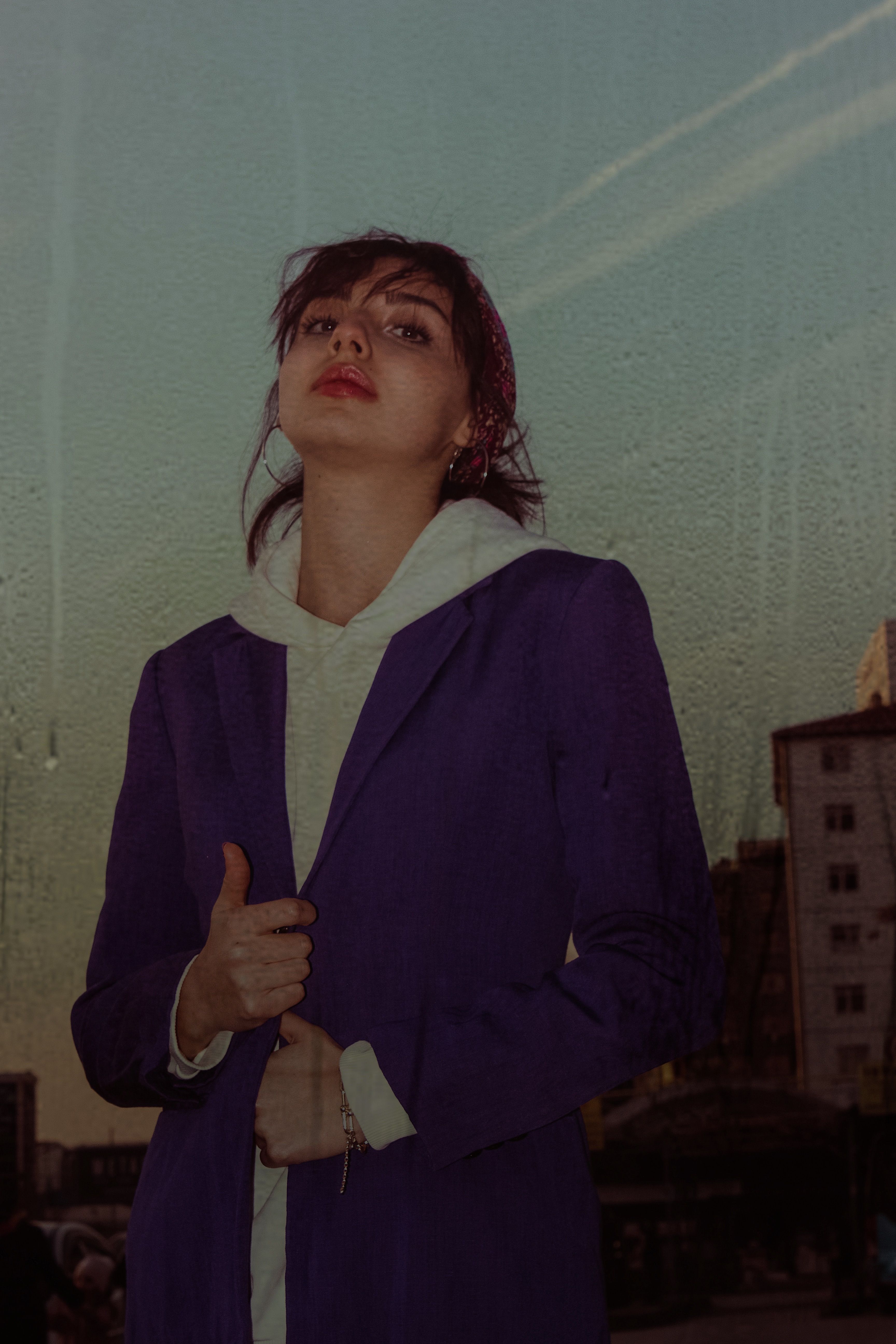 A woman in a purple coat poses confidently against an urban Ankara backdrop at dusk.