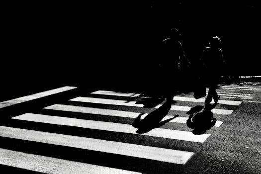 High contrast black and white image of people walking across a street in silhouette at night.