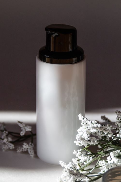 Free A sleek cosmetic bottle surrounded by white flowers, perfect for beauty and skincare themes. Stock Photo