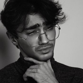 A close-up black and white portrait of a young man in eyeglasses, deep in thought.