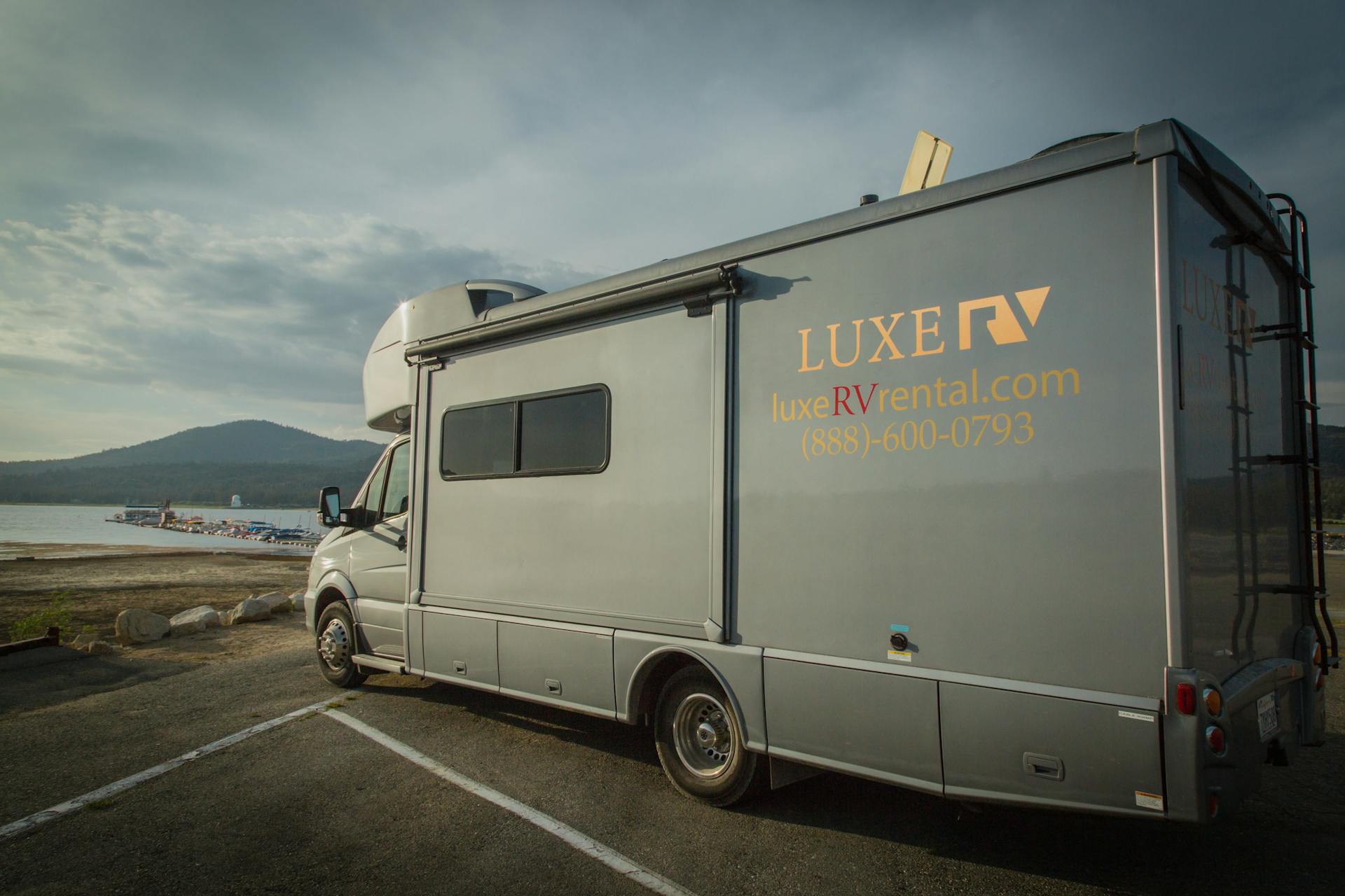 A luxury RV parked by a scenic lake shore with mountains in the background. Perfect for travel enthusiasts.