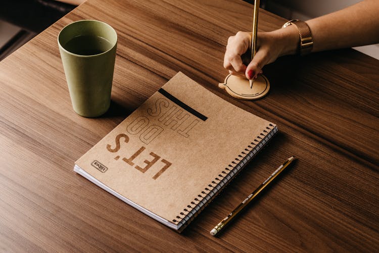 Note Pad Lying On A Wooden Desk And A Hand Of A Woman Drawing On A Paper Speech Bubble