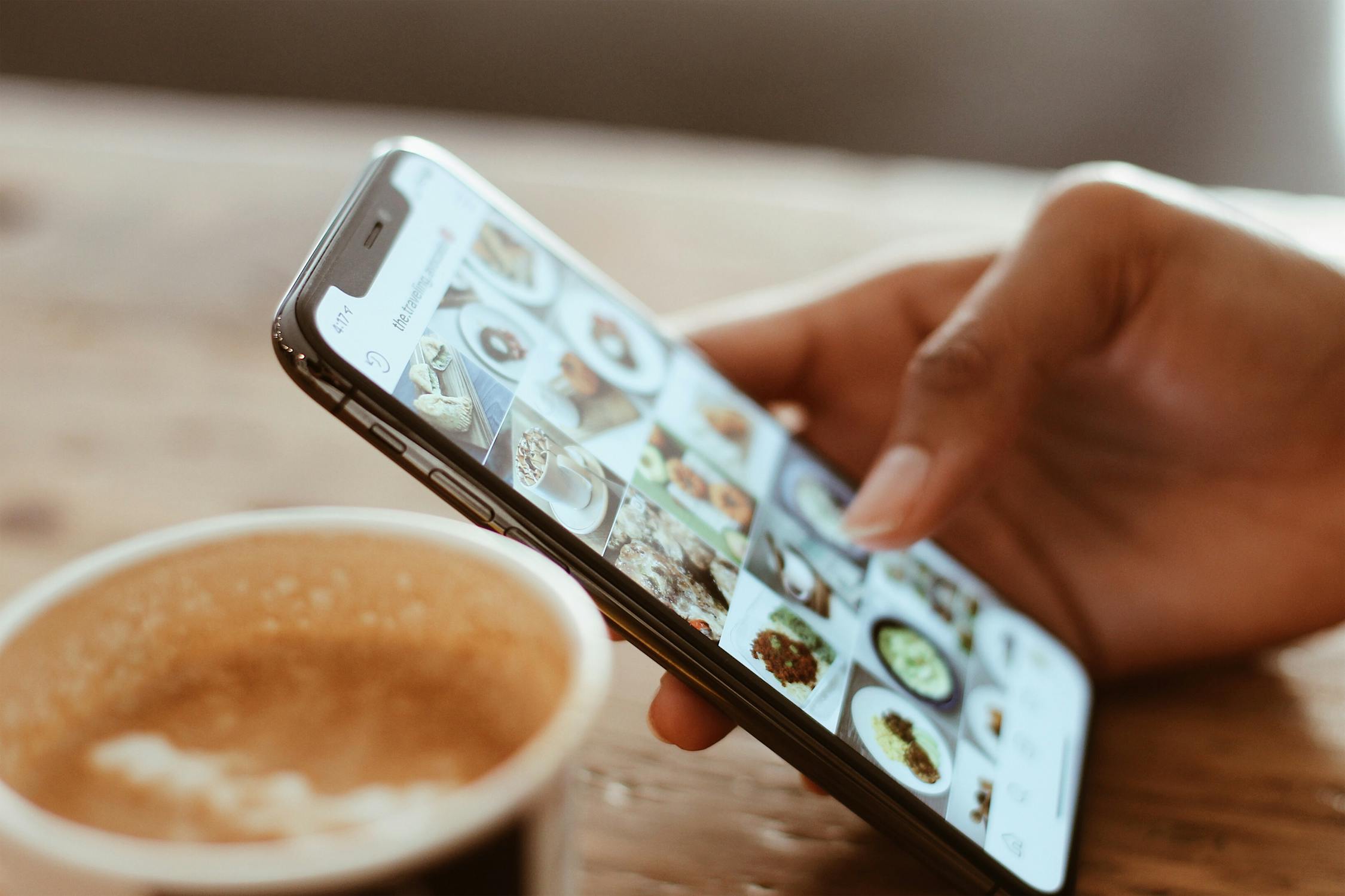 Hand holding mobile phone with images displayed and coffee in the background pros and cons of instagram