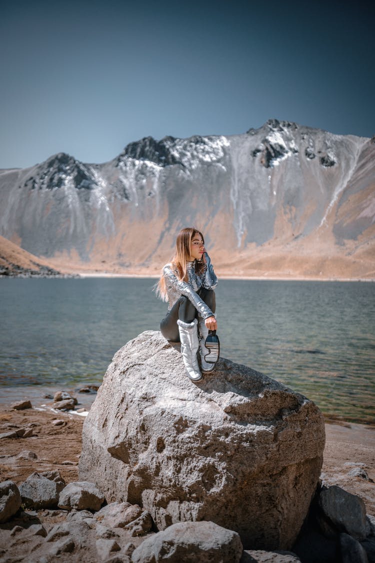 Fashion Model Sitting On Rock In Mountains Landscape