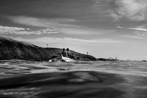 Black and White Photo of Men Kayaking by Sea Shore