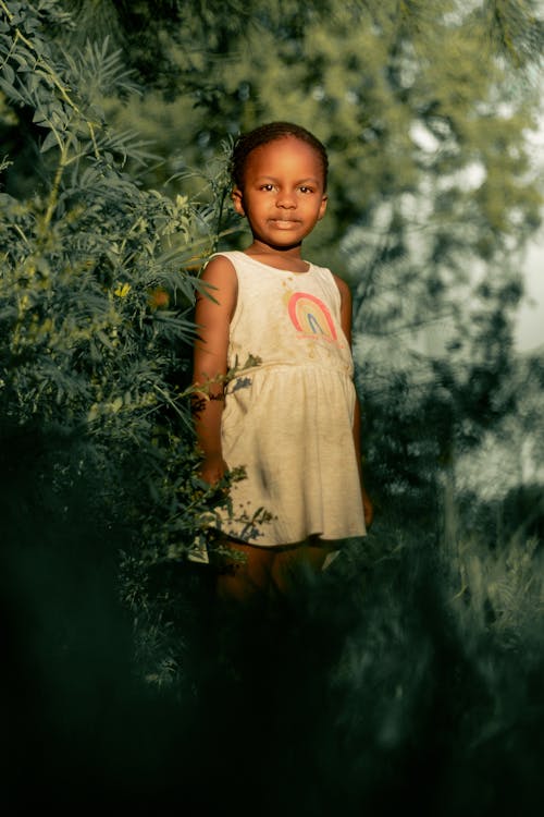 Little Girl in Yellow Dress Standing among Bushes