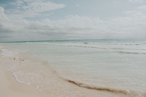 Free Serene beach scene with gentle waves lapping against the shore under a cloudy sky. Stock Photo