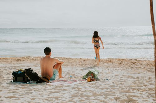 Free Man relaxing on the beach with a girl running towards the ocean waves. Perfect holiday scene. Stock Photo