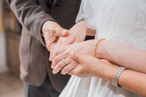 Free A close-up of a bride and groom holding hands, showcasing elegant jewelry and wedding attire. Stock Photo