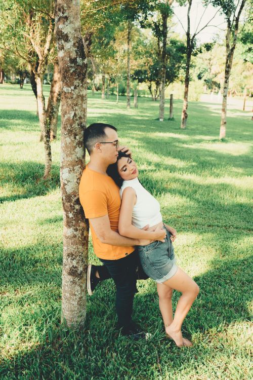 Free A loving couple embraces against a tree in a sunlit park, radiating warmth and connection. Stock Photo