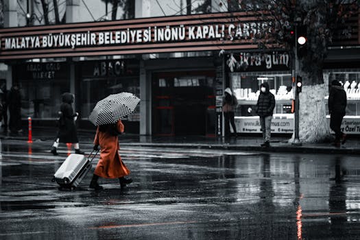 A woman in an orange coat walking in the rain with an umbrella on a city street.