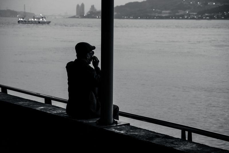 Black and white silhouette of a man sitting on a pier by the water, peaceful and reflective.