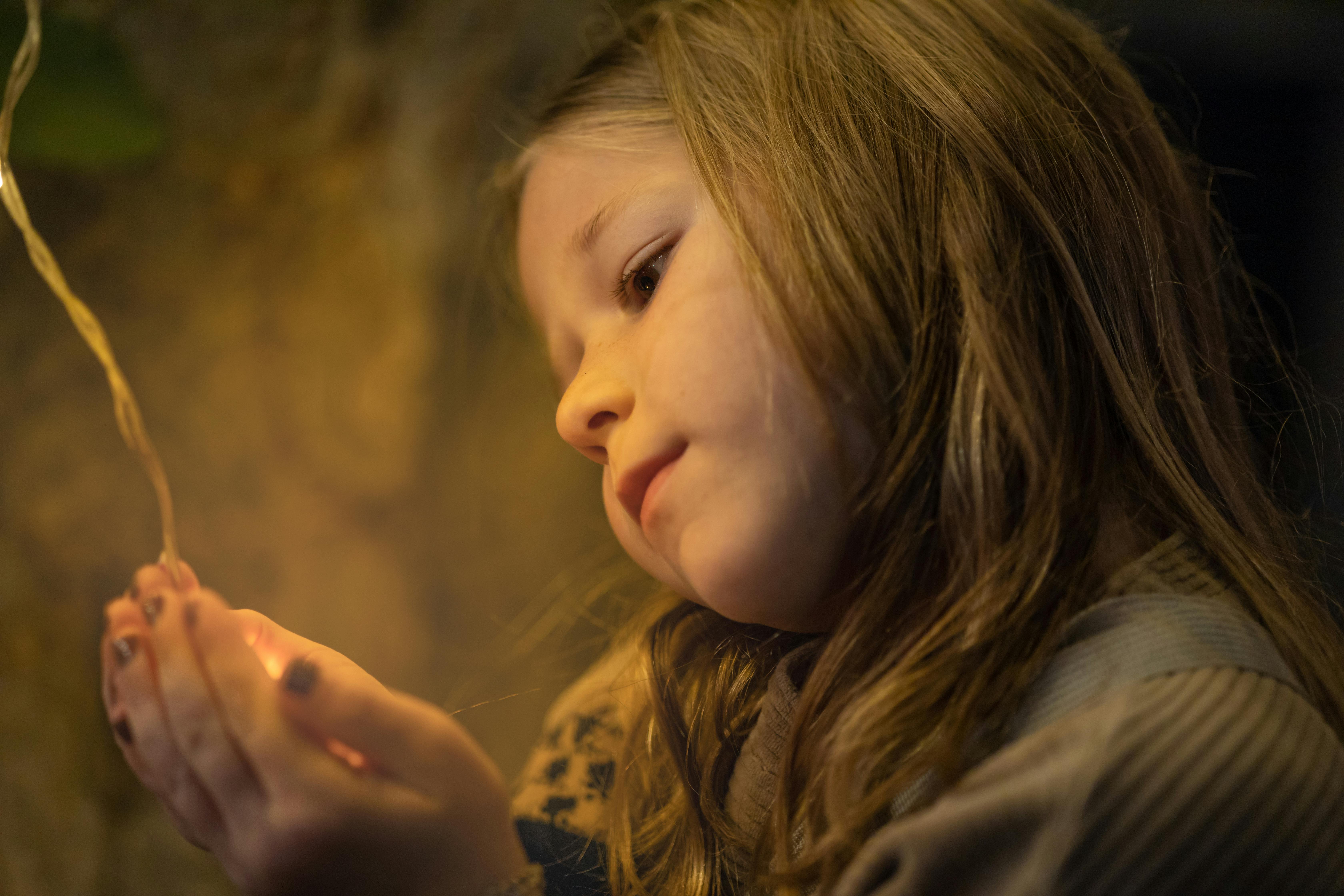 A young girl gently holds string lights, creating a warm and contemplative mood.