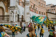 Vibrant flag parade in an old town square featuring performers amidst historic architecture.