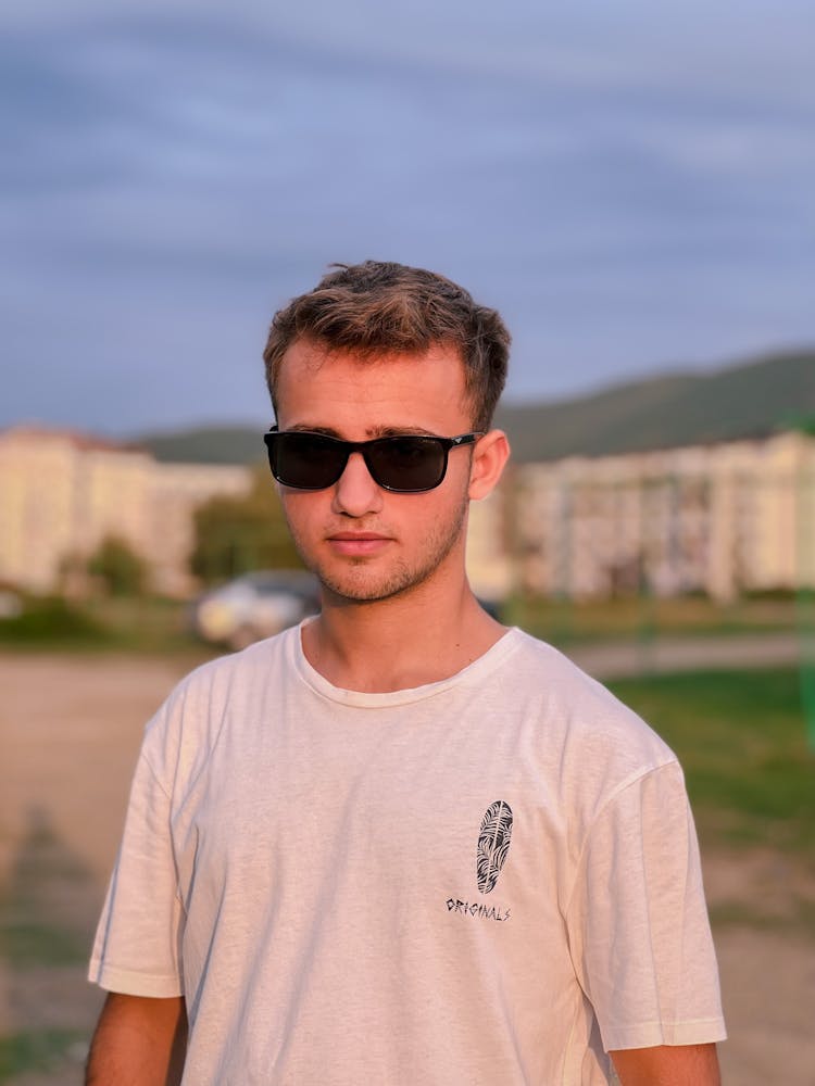 Young Man In A White T-shirt And Sunglasses Standing Outside 