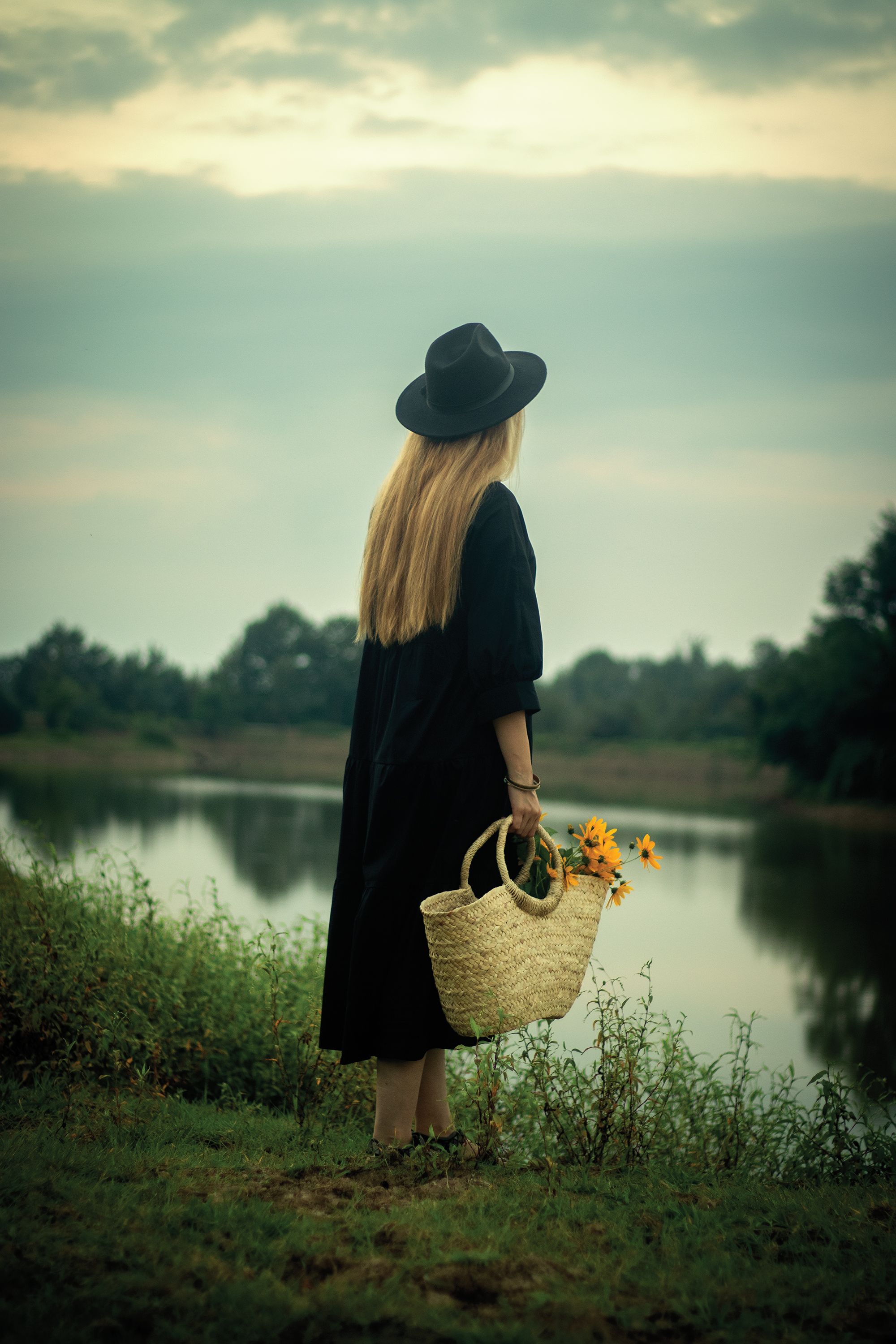 Back View of a Woman Standing with a Basket with Flowers by a Body of ...