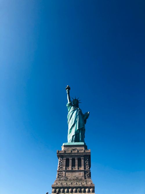 Free Iconic Statue of Liberty with a vivid blue sky highlighting its grandeur in New York City. Stock Photo