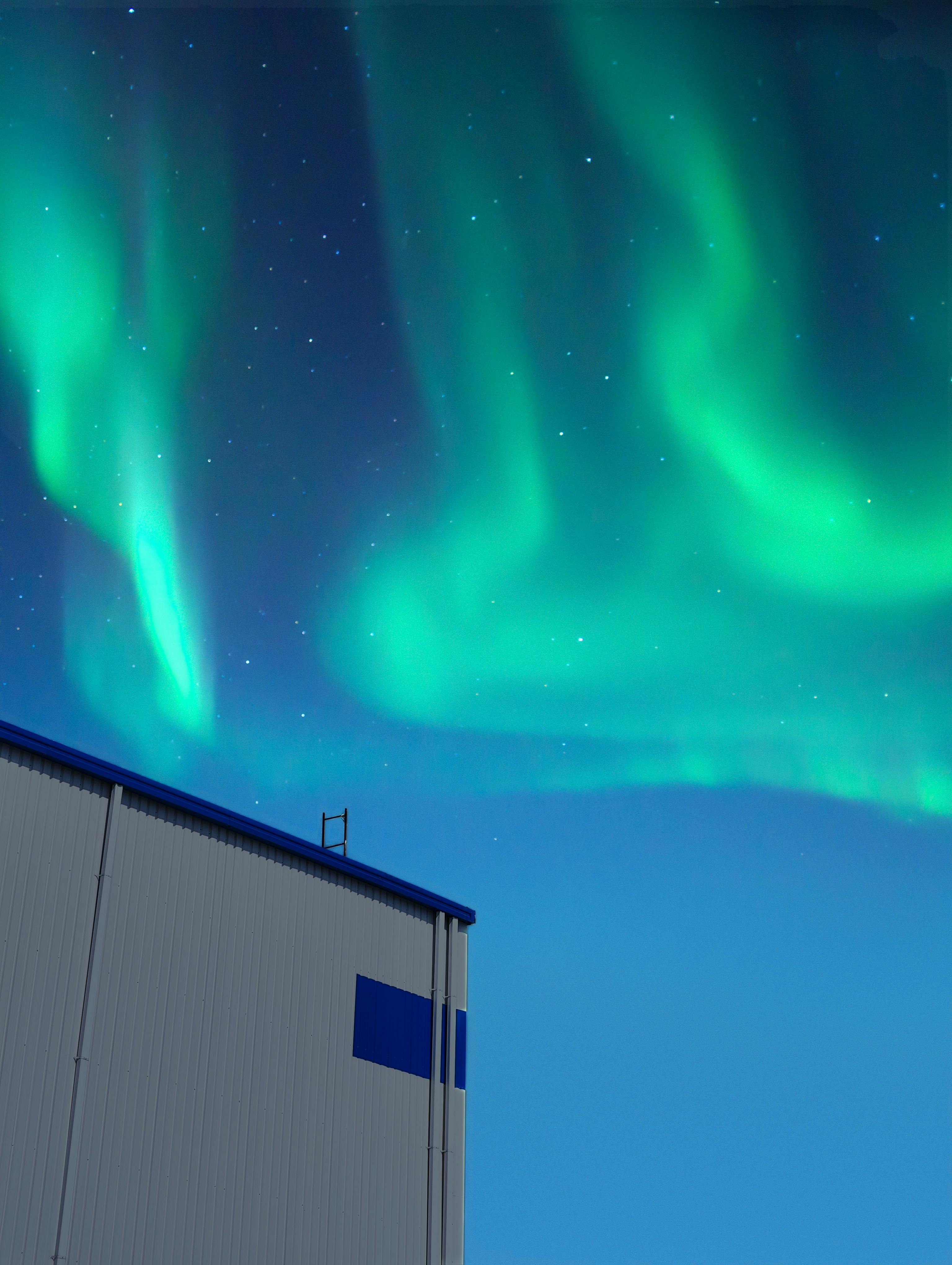 Stunning Northern Lights illuminate night sky above a modern industrial building.