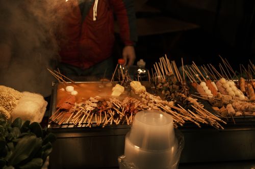 Free A vibrant display of various skewered meats cooking at a bustling night market food stall. Stock Photo