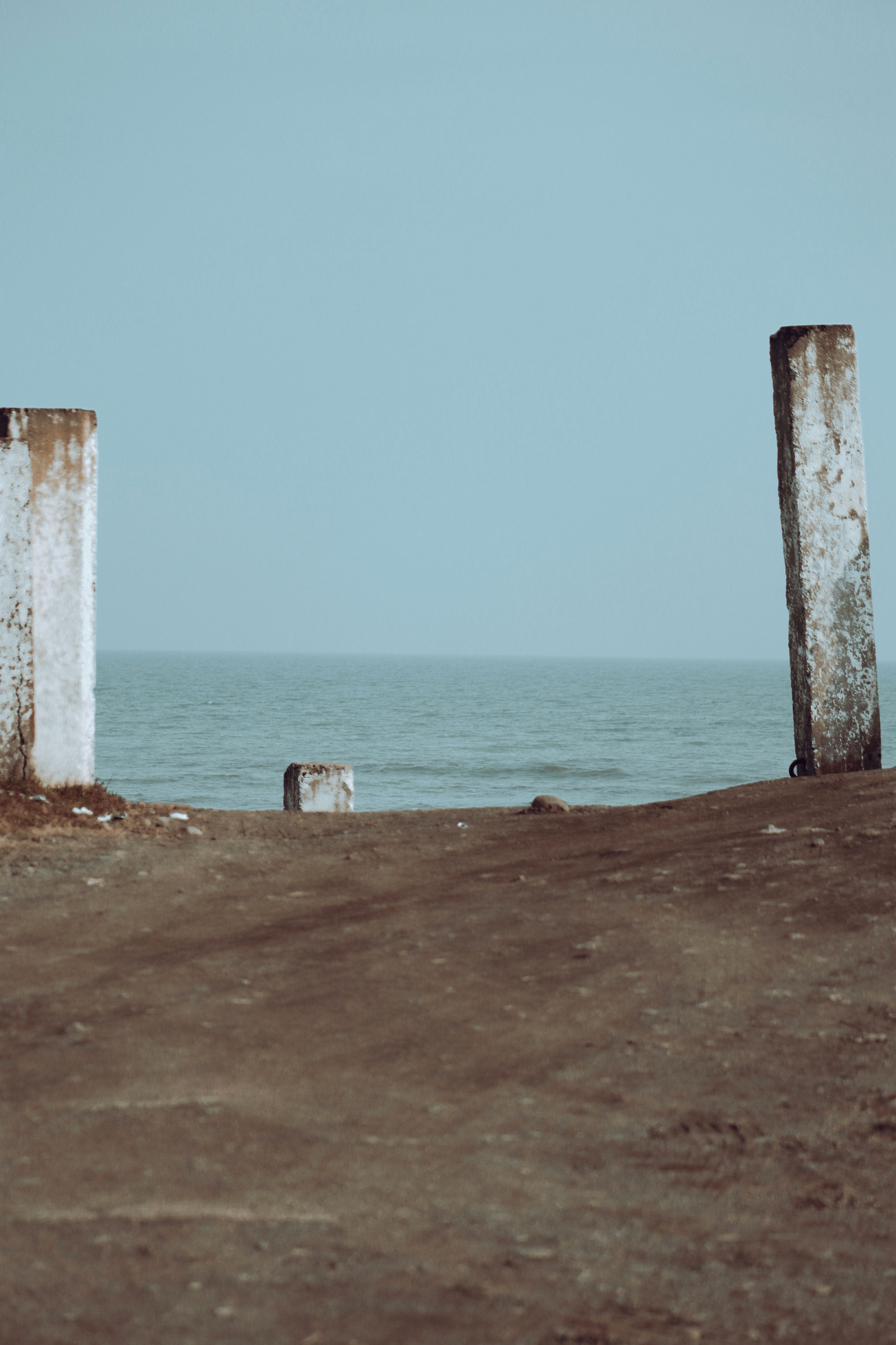 Rustic beach scene with two weathered pillars leading to a calm ocean view.