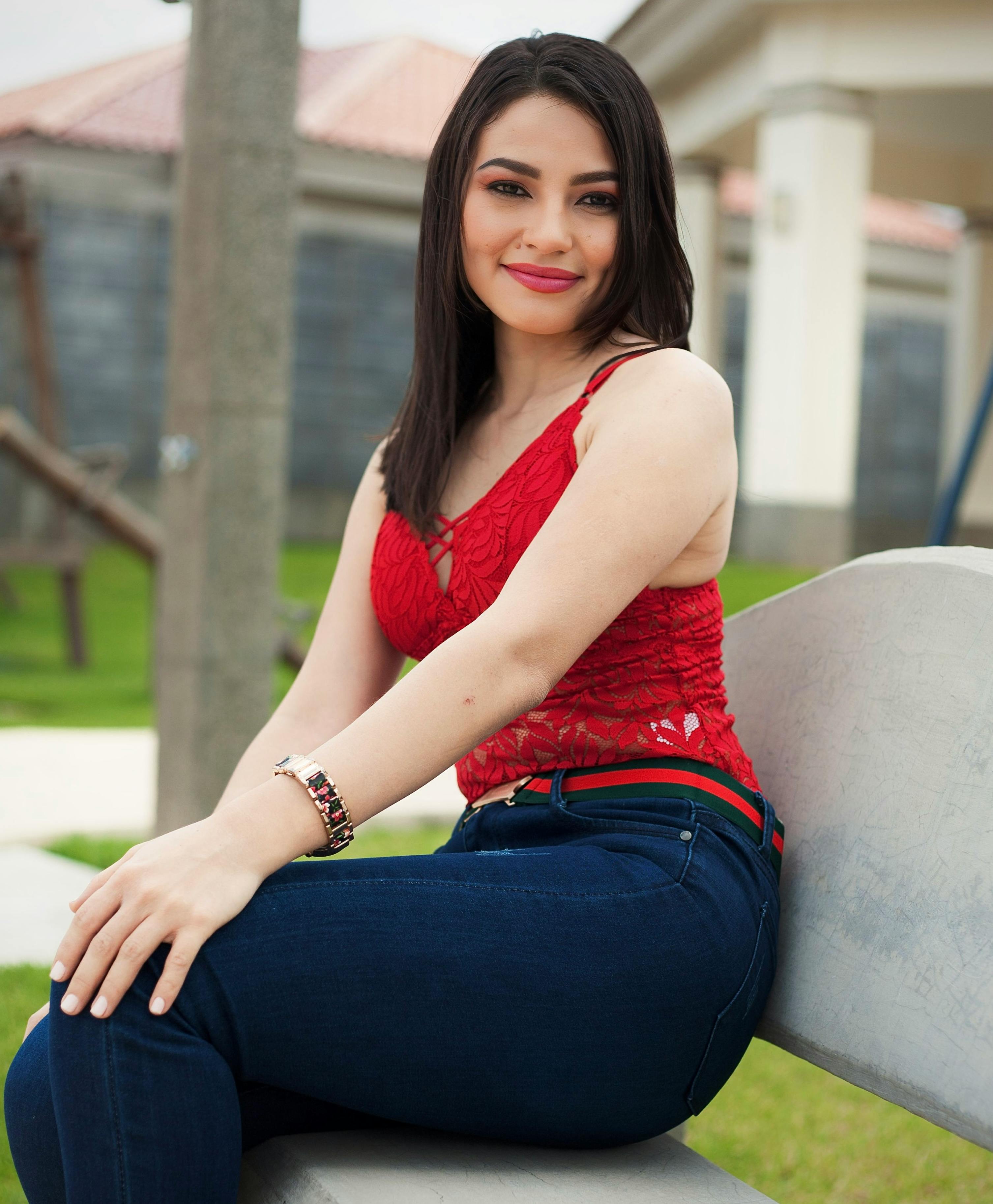 Stylish woman in jeans and red lace blouse, posing outdoors in Managua, Nicaragua.