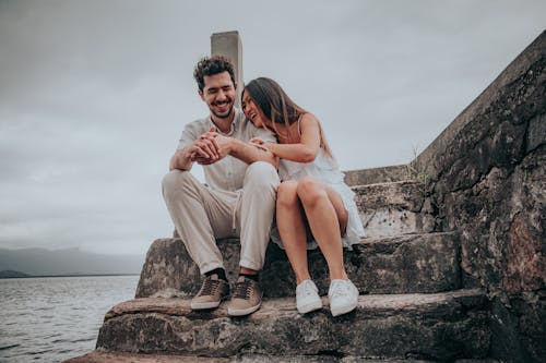 Couple Sitting Together on a Rocky Staircase by the Sea and Laughing