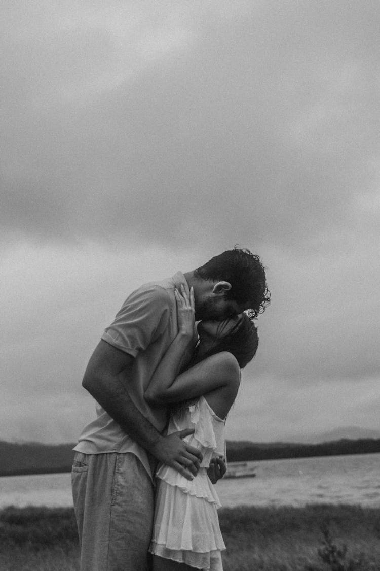 Couple Kissing And Hugging In Front Of A Cloudy Sky In Black And White