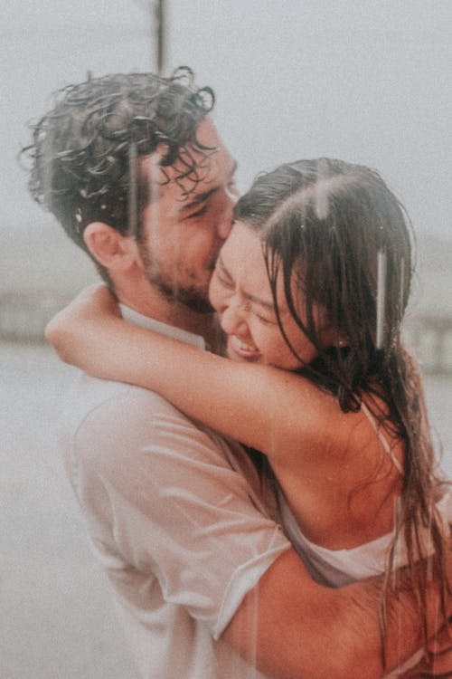 A Couple Hugging and Smiling in the Rain 