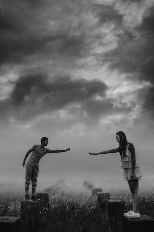 Black and White Photo of a Man and Woman Standing Outside and Reaching Their Arms Toward Each Other 