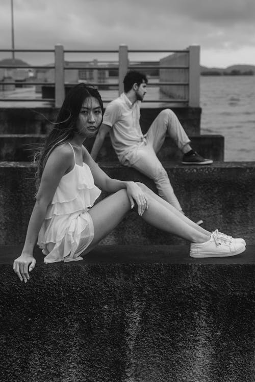 Woman in Sundress and Man Sitting on Walls on Shore in Black and White