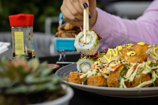 Close-up of a hand holding sushi with chopsticks over a vibrant sushi platter on a dark background.