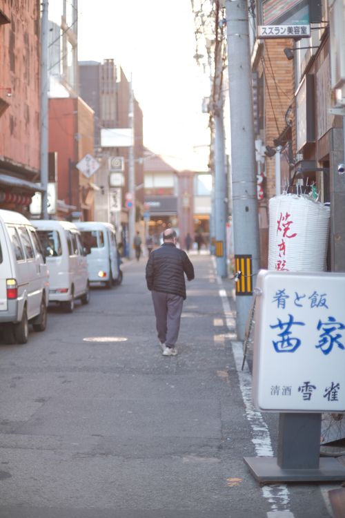 Free A man walks down a street lined with vehicles and signs in Japan. Stock Photo