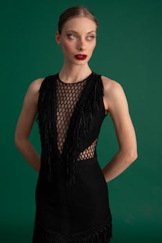 Stylish portrait of a woman in a black mesh and fringe dress against a green background.