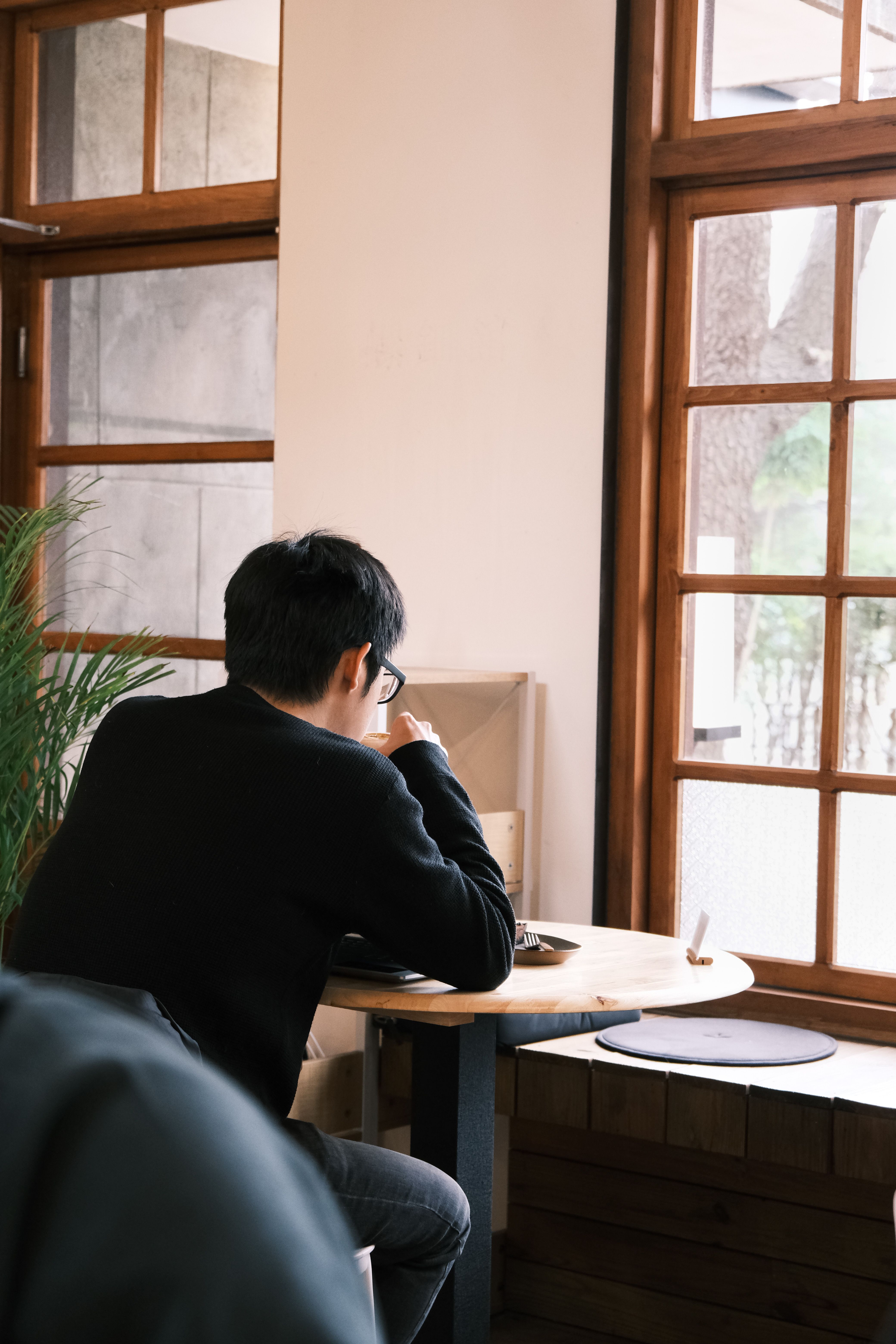 A man in a cafe enjoys solitude by large windows, creating a serene atmosphere.