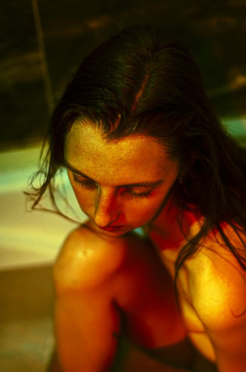 Free A woman with brunette hair sits thoughtfully in a bathtub under warm, moody lighting. Stock Photo