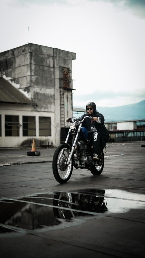 Free A motorcyclist rides an urban street with reflections on a wet surface, exuding a sense of adventure. Stock Photo