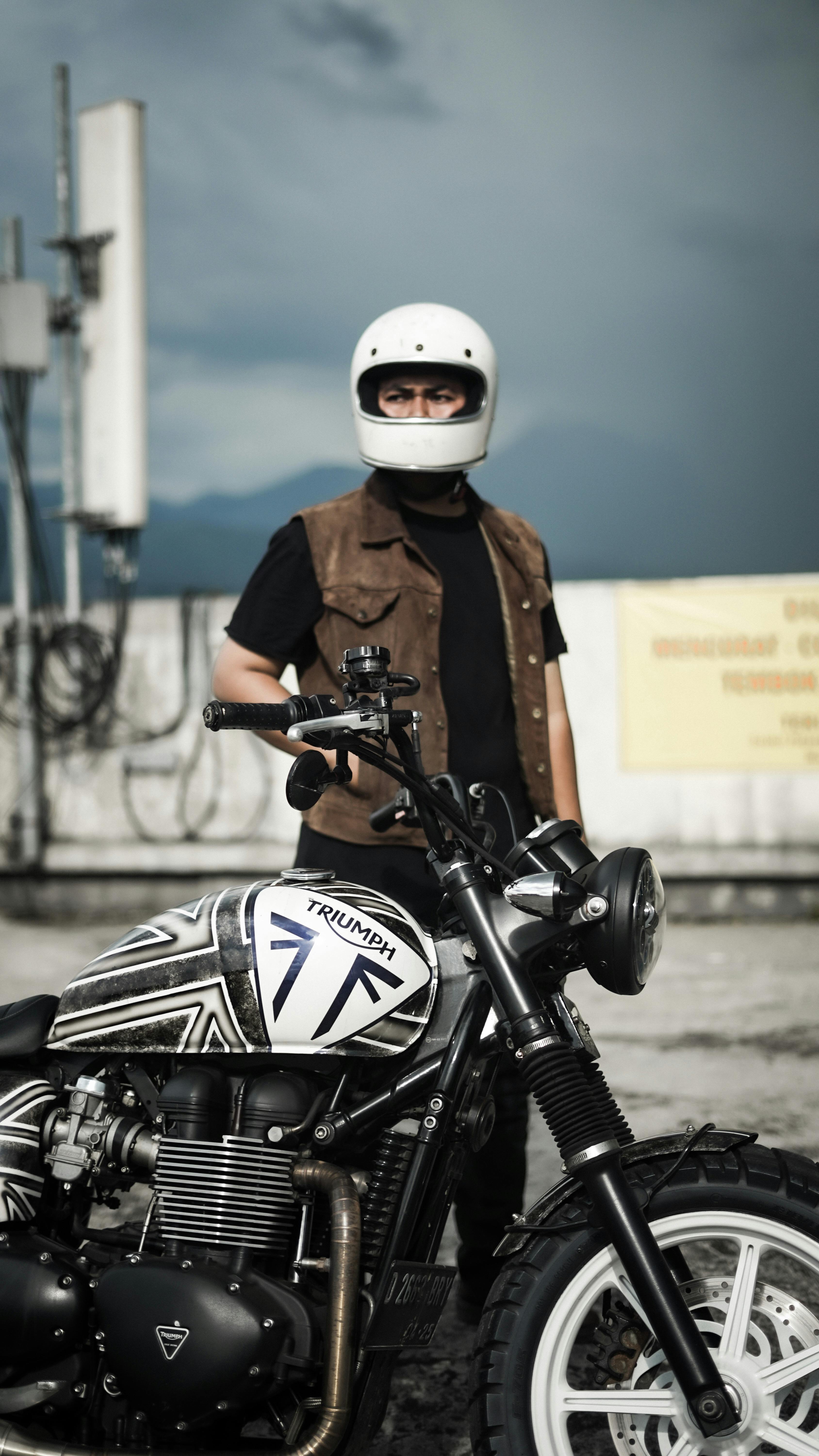 Man in helmet poses with custom Triumph bike, capturing urban adventure vibe.