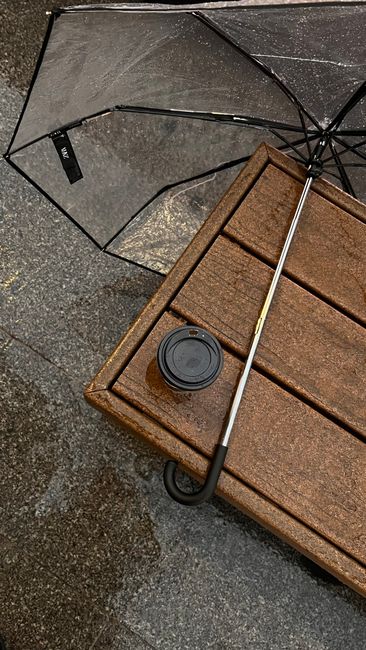 A top-down view of an umbrella and takeaway cup on wet pavement, ideal for urban lifestyle concepts.