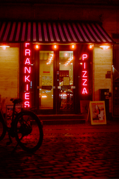 Vibrant neon-lit pizza shop entrance at night in Copenhagen, Denmark.