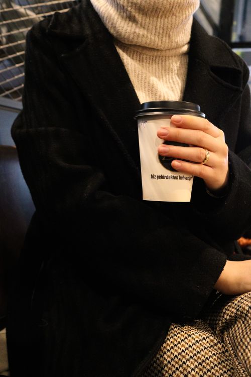 Free Close-up of a woman holding a coffee cup indoors, wearing a turtleneck and coat. Cozy and stylish setting. Stock Photo