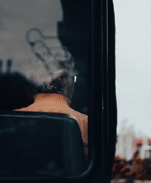 Free A candid view of an elderly woman sitting on a bus, seen from behind through the window. Stock Photo