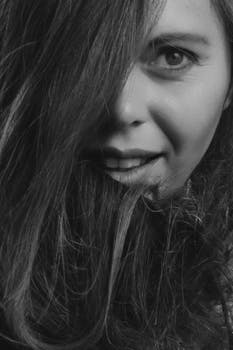 这是一张黑白特写肖像，画中的女人长发遮住一只眼睛，正热情地微笑着