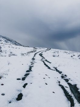 Snowy mountain landscape with overcast skies featuring a winding trail leading uphill.