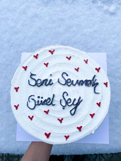 Free White frosted cake with red hearts and handwritten text on a snowy background. Stock Photo