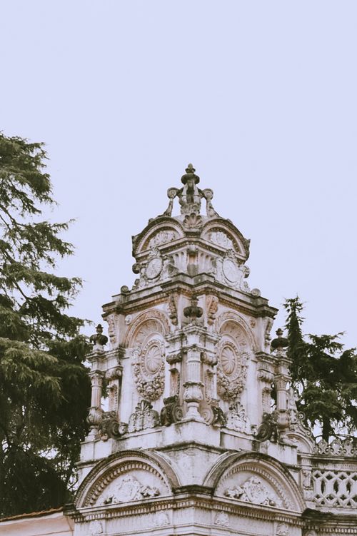 Free Close-up of an ornate historic tower surrounded by lush trees on a clear day. Stock Photo