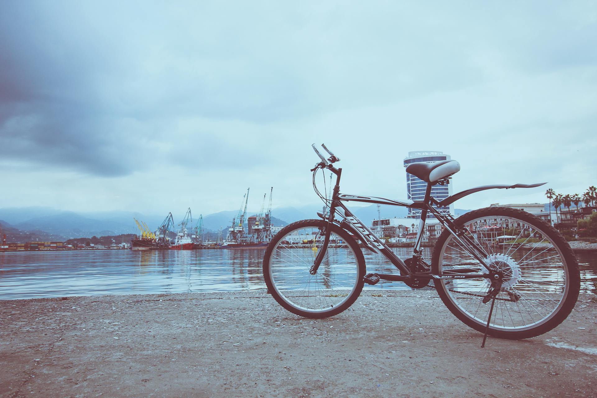 A solitary bicycle parked by a serene seaport under cloudy skies, showcasing urban coastal life.